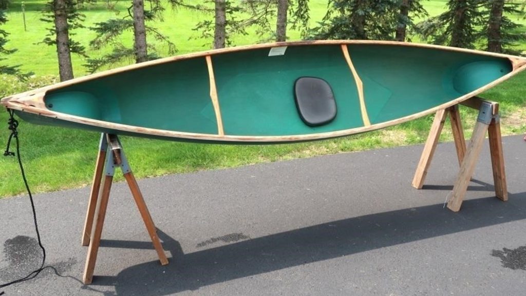 A simple one-person canoe with a wooden frame and turquoise interior propped on its side atop a pair of sawhorses.