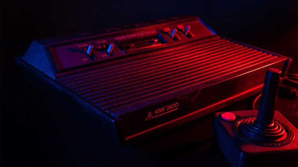 Atari 2600 "VCS" game system from 1977, displayed in low red light  with a joystick controller.