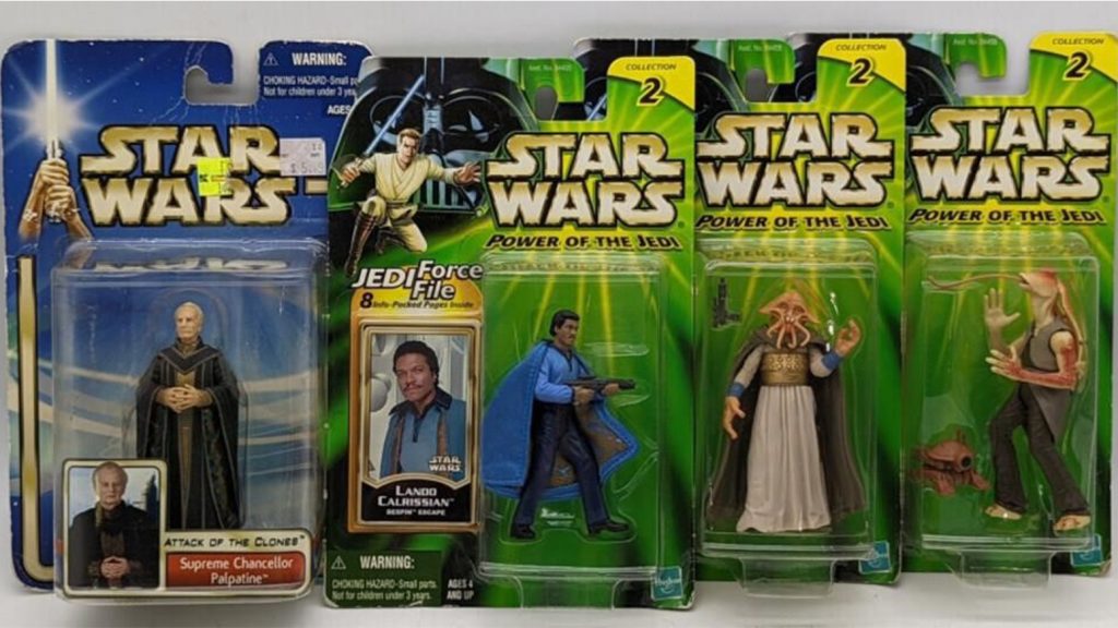 One action figure in blue packaging and three figures in green packaging propped on a white surface. 