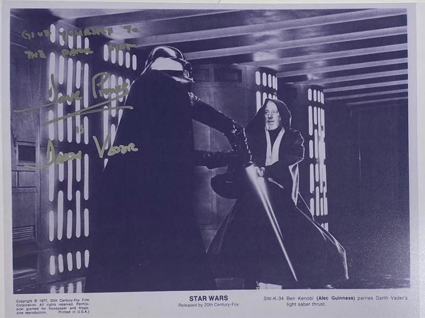 Black and white photo of characters Ben Kenobi and Darth Vader parrying with light sabers. 