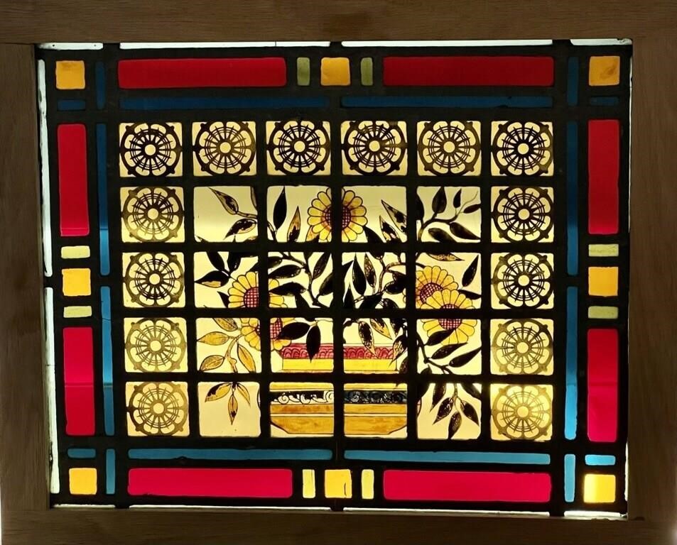 A framed stained-glass piece with red, yellow, green, and blue rectangles framing square pieces with a round mandala design.